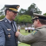 Cel Nivaldo Restivo recebe medalha em seu peito de outro oficial, observado por outro companheiro.