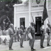 Grupo de homens da brigada, uniformizados, em formação, em frente a um prédio com um letreiro escrito "Pedro e Paulo".