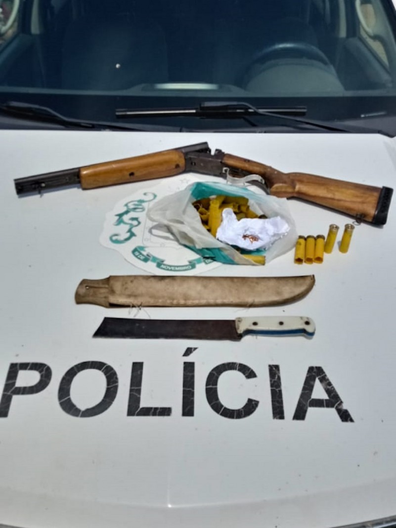 Materiais apreendidos sendo uma espingarda e cartuchos de arma de fogo. Ao lado um fac&atilde;o e uma bainha.