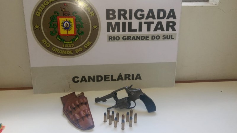 No fundo o banner da Brigada Militar. Sobre uma mesa uma arma de fogo e muni&ccedil;&otilde;es.