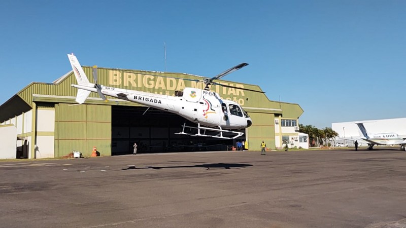 Foto do helicóptero da Brigada Militar levantando voo na frente do hangar da BM no aeroporto.