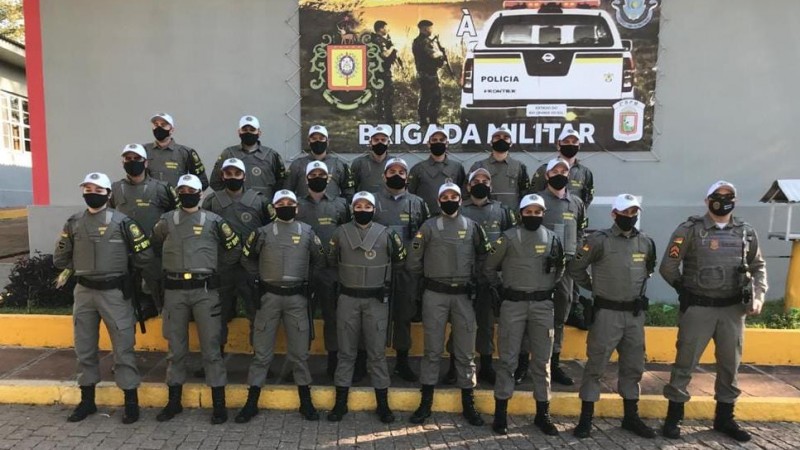 Alunos soldados do Polo de ensino Rio Pardo equipados, juntamente com o instrutor 1&ordm; Sargento Dias em frente a um banner da Brigada Militar.