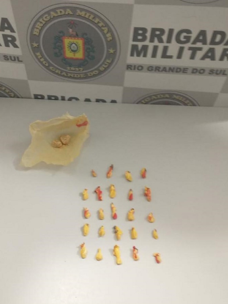 Ao fundo o banner da Brigada Militar. Sobre uma mesa drogas fracionadas apreendidas.