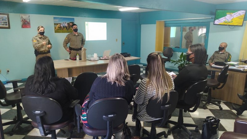 Policiais Militares palestrando frente de quatro mulheres em uma sala.