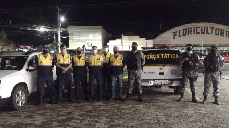 Tr&ecirc;s policiais militares da for&ccedil;a t&aacute;tica a frente de uma viatura policial, e ao lado seis agentes de tr&acirc;nsito perfilados.