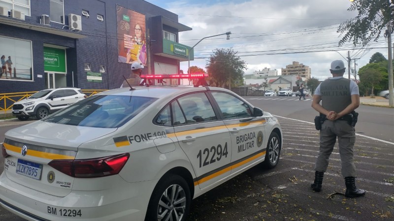 Um policial militar ao lado de uma viatura policial militar com os giros flash ligados.