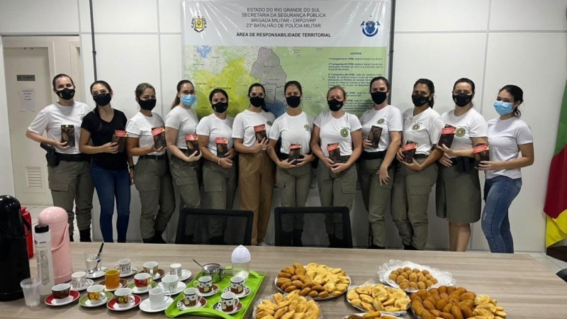Polciais militares femininas perfiladas com a bandeira do Estado do Rio Grande do Sul ao lado e uma mesa a frente