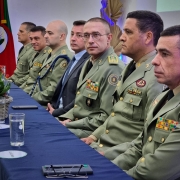 Cinco militares e um civil estão sentados lado a lado atrás de uma mesa com toalha azul escura