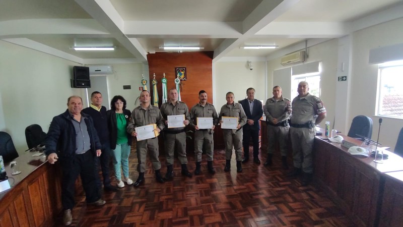 A fotografia mostra diversas pessoas, políticos e policiais militares. Os policiais militares estão com certificados em mãos, que receberam em homenagem ao seu trabalho realizado. 