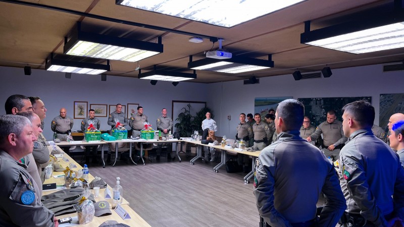 Foto mostra mesa de reunião com coronéis em pé durante apresentação