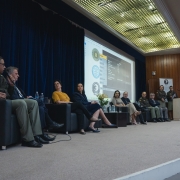 Imagem mostra participantes sentados em um palco, palestrando durante o evento