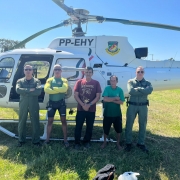 Foto mostra integrantes do Batalhão de Aviação junto aos resgatados, na frente a um helicóptero