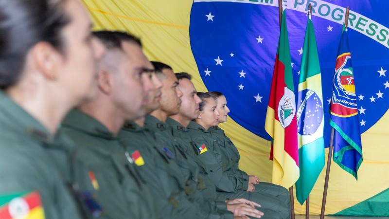 Foto mostra os formandos sentados em fileira. Em segundo plano, estão as bandeiras do Brasil, do Rio Grande do Sul e da Aviação da Brigada Militar.