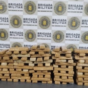 porções de maconha empilhadas com o brasão da Brigada Militar ao fundo