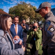Soldado recebe o carinho da esposa e do filho récem nascido. ao fundo estão o governador, o secretário adjunto de segurança pública e fotógrafos