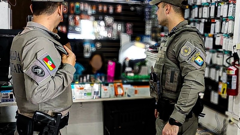 Dois policiais militares em fiscalização em uma loja de celulares.