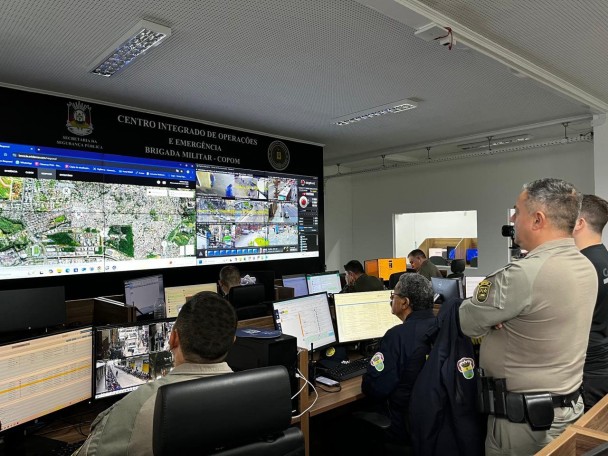 Quatro policiais militares analisando telas de televisão na estrutura do COPOM.