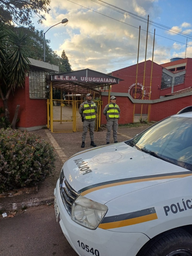 Foto mostra dupla de policiais militares posicionados em frente ao portão de uma escola