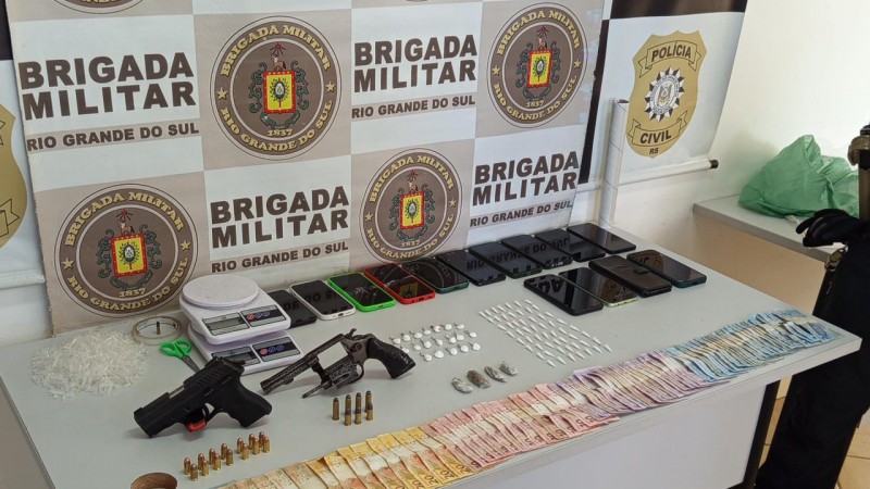 Mesa expõe a materialdiade apreendida pelos policiais. Há um banner das polícias PC e BM ao fundo, na parede.