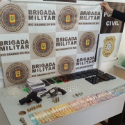 Mesa expõe a materialdiade apreendida pelos policiais. Há um banner das polícias PC e BM ao fundo, na parede. 