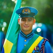 Jovem estudante, sorridente, aparece fardado e carregando a bandeira brasileira