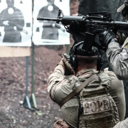 dois PMs armados apontam armas ao alvo que é um desenho à distância, desenho de uma pessoa da cintura pra cima