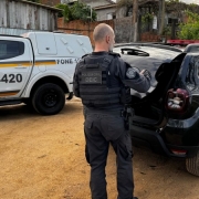 dois policiais militares e um policial civil, duas viaturas, sendo uma de cada polícia, em uma rua ou pátio com chão de terra
