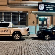 duas viaturas estacionadas numa rua, uma da BM e outra da PC, em frente à uma Delegacia de Polícia