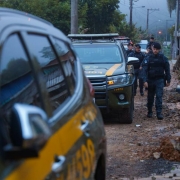 numa rua de chão batido, entre as viuaturas da BM e a cerca de moradias humildes, vem em fila policiais