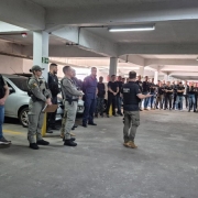 grande círculo de policiais militares e policiais civis reunidos em um estacionamento fechado