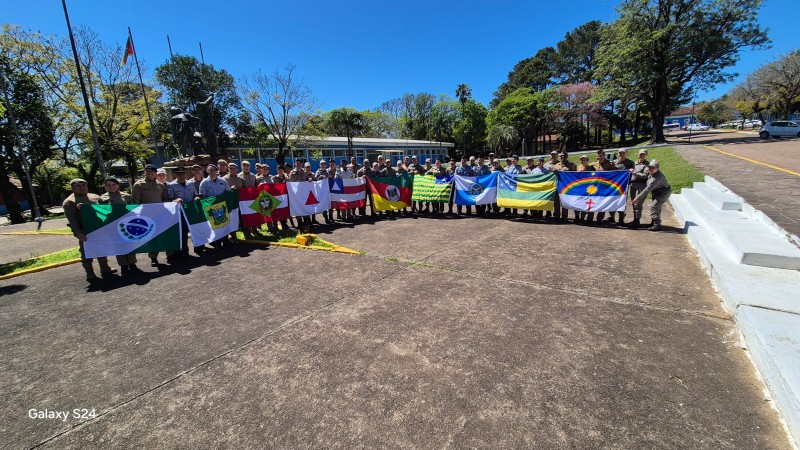 alunos do curso num estacionamento sob o sol segurando as bandeiras dos estados da federação 