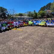 alunos do curso num estacionamento sob o sol segurando as bandeiras dos estados da federação 