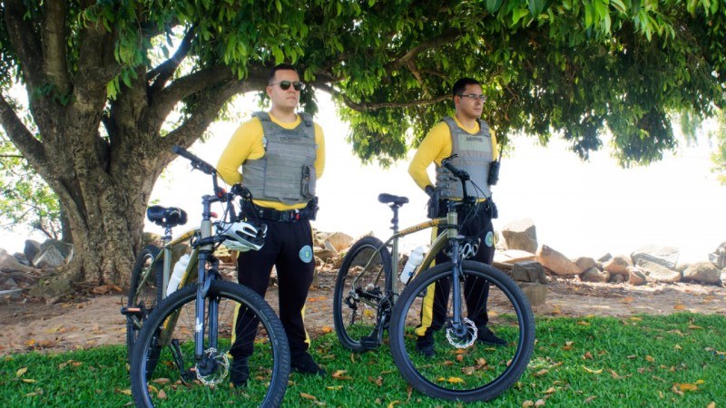 dois policiais militares com bicicletas em uma parque sob uma árvore