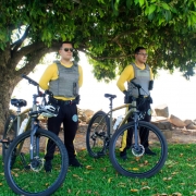 dois policiais militares com bicicletas em uma parque sob uma árvore