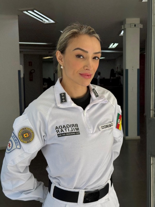 PM entrevistada, com farda branca, em pé, mãos para trás, cabelo preso, no hall do hospital