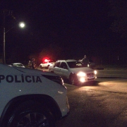 Veículos da PM aparecem com poucas luzes, à noite, e algumas pessoas, durante fiscalização