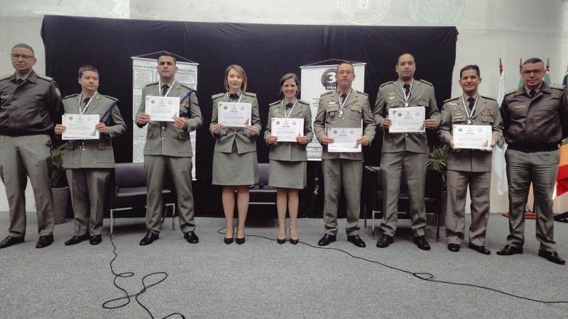 PMs formados aparecem em fileira ostentando o diploma. À esquerda, está o chefe do do IPBM, major PM Michel Ribeiro, e à direita, o diretor de Ensino da Brigada Militar, coronel PM Jorge Dirceu Abreu Silva Filho