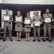 PMs formados aparecem em fileira ostentando o diploma. À esquerda, está o chefe do do IPBM, major PM Michel Ribeiro, e à direita, o diretor de Ensino da Brigada Militar, coronel PM Jorge Dirceu Abreu Silva Filho