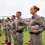PM feminina em primeiro plano. Fileiras de PMs dispostos no campo da APM durante solenidade