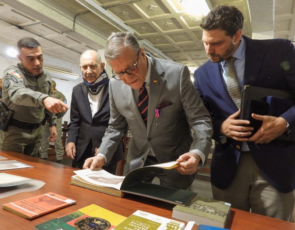 Todos em pé, em frente a uma mesa, na qual estão dispostos livros antigos. O neto do Patrono folheia o Álbum comemorativo aos 30 anos da Instituição. 