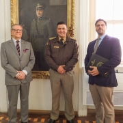 Os três homens estão em pé e à frente do quadro com a imagem do Coronel Massot, o Patrono da BM