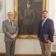 Neto e bisneto do Patrono aparecem em frente ao quadro que homenageia o antepassado, no Salão Nobre do Prédio do Estado-Maior da BM