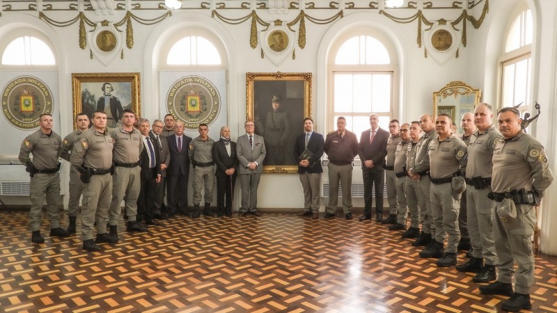 Militares e membros do Conselho Superior da BM formam um semicírculo. No centro está o quadro com a imagem do Coronel Massot e o neto e o bisneto, um de cada lado do Patrono da Instituição.  
