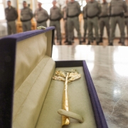 Em primeiro plano, aparece o objeto em ouro, que tem a forma de um ramo de oliveira. Ao fundo, estão militares presentes à solenidade. 