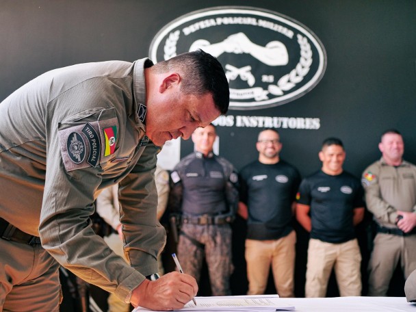 Coronel Luigi assina o documento de lançamento do Manual. Ao fundo aparecem os instrutores, formados no primeiro curso.