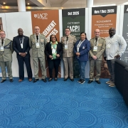 Foto mostra os quatro integrantes da comitiva da Brigada Militar posando para foto junto a uma comitiva estrangeira. Por trás deles, estão cartazes da feira IACP 2025