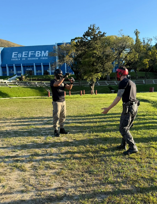 Dupla de PMs em pé, em frente um do outro, durante um simulado no campo da Academida de Polícia
