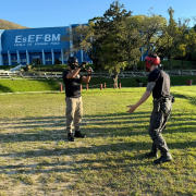 Dupla de PMs em pé, em frente um do outro, durante um simulado no campo da Academida de Polícia 
