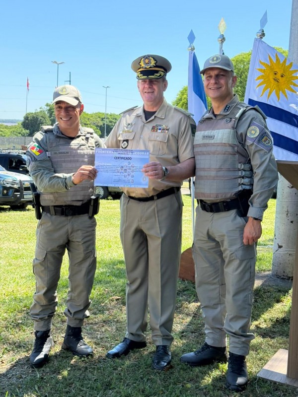 Três autoridades da segurança pública brasileira aparecem em pé exibindo um certificado. 