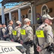 PMs aparecem em fileira, de costas e diante de um prédio histórico.